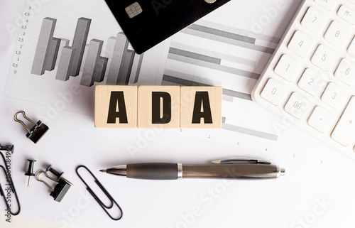 ADA acronym on wooden blocks with financial charts, calculator, pen and office supplies