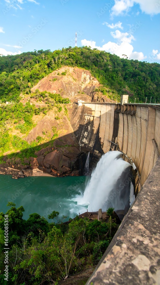 Obraz premium Dam waterfall, green hills, blue water