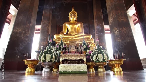 Golden Buddha Statue in Dark Temple Interior with Floral Offerings
