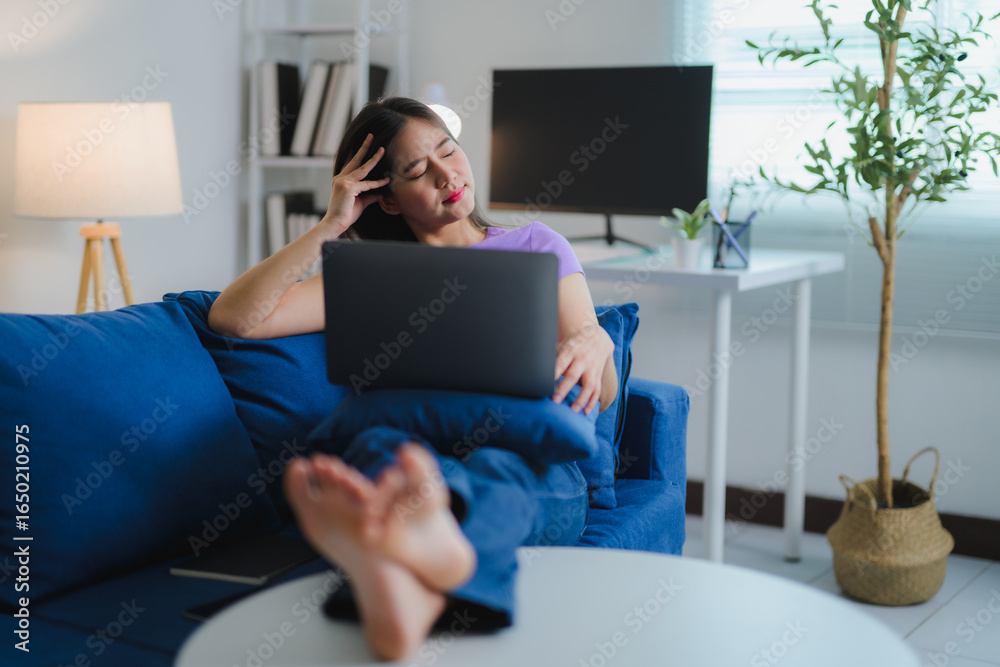 Tired freelancer woman taking a break on the couch with laptop on knees Tired freelancer woman taking a break on the couch with laptop on knees