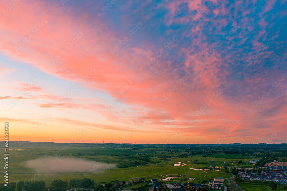 Fototapeta premium Expansive Grassland under Radiant Sunset Sky Filled with Evening Clouds