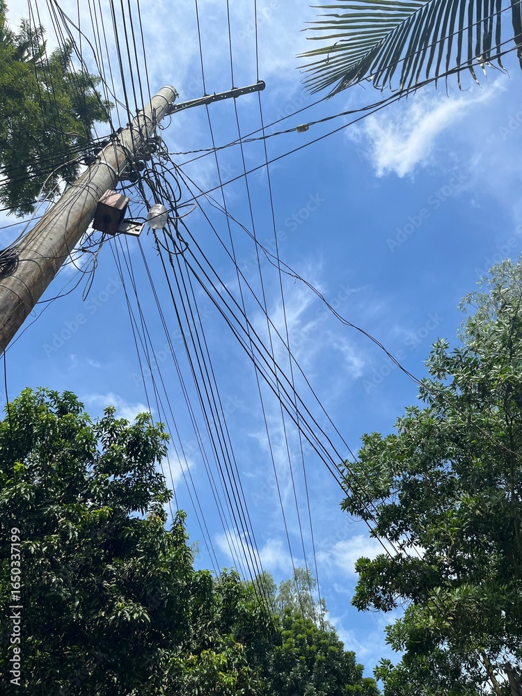 Obraz premium Electric pole with power lines against clear blue sky and green trees, rural energy infrastructure in natural landscape, countryside electricity connection with scenic outdoor view for technology blog