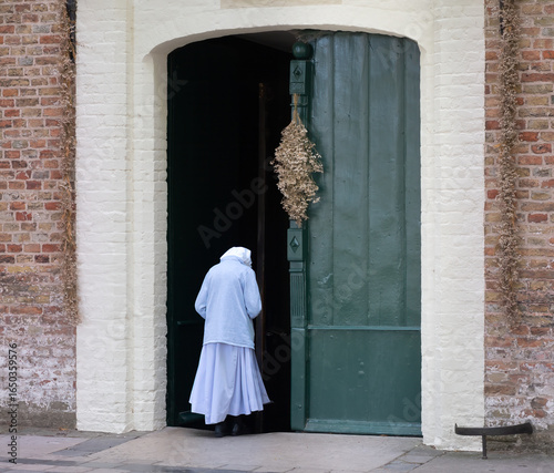 A beguine enterring the church of the Beguinage in the old city of Bruges (Brugge), East Flanders, Belgium. The is a centuries old lay sisterhood in the Low Countries of Europe
