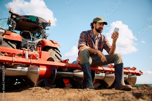 Bild auf Leinwand Below view of farmer using smart phone while taking a break from working in the field