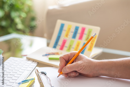 Teacher writing on clipboard while planning school activities using a flow chart made with sticky notes and a pencil, promoting organization, education, and successful learning