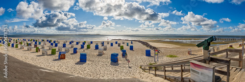 Fast menschenleerer Strand von Utersum auf der Nordseeinsel Föhr mit Strandkörben, und der von leichter Bewölkung verdeckten Sonne im Gegenlicht