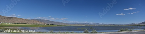 Panoramic view of a serene lake bordered by distant mountains under a clear blue sky