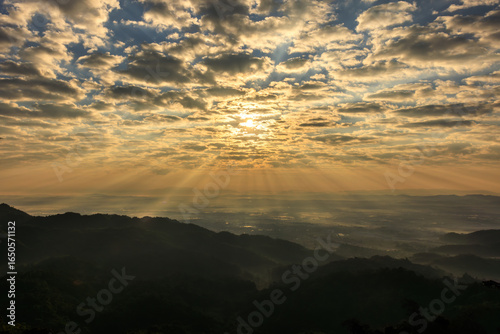 Sunbeams pierce through dramatic clouds over the valley at morning time,