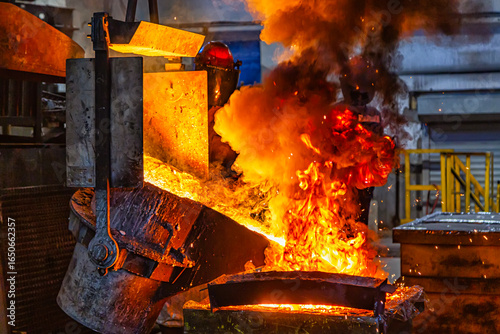 A man in a fireproof suit and helmet turns over molten burning metal with fiery splashes from a ladle, which pours out in a fiery stream from a metallurgical furnace