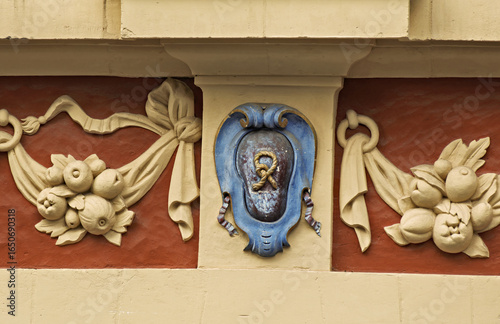 Tableau sur toile Close-up of an ornate architectural detail on a historic building facade, featuring a central blue cartouche with a decorative motif and surrounding fruit garlands in beige relief