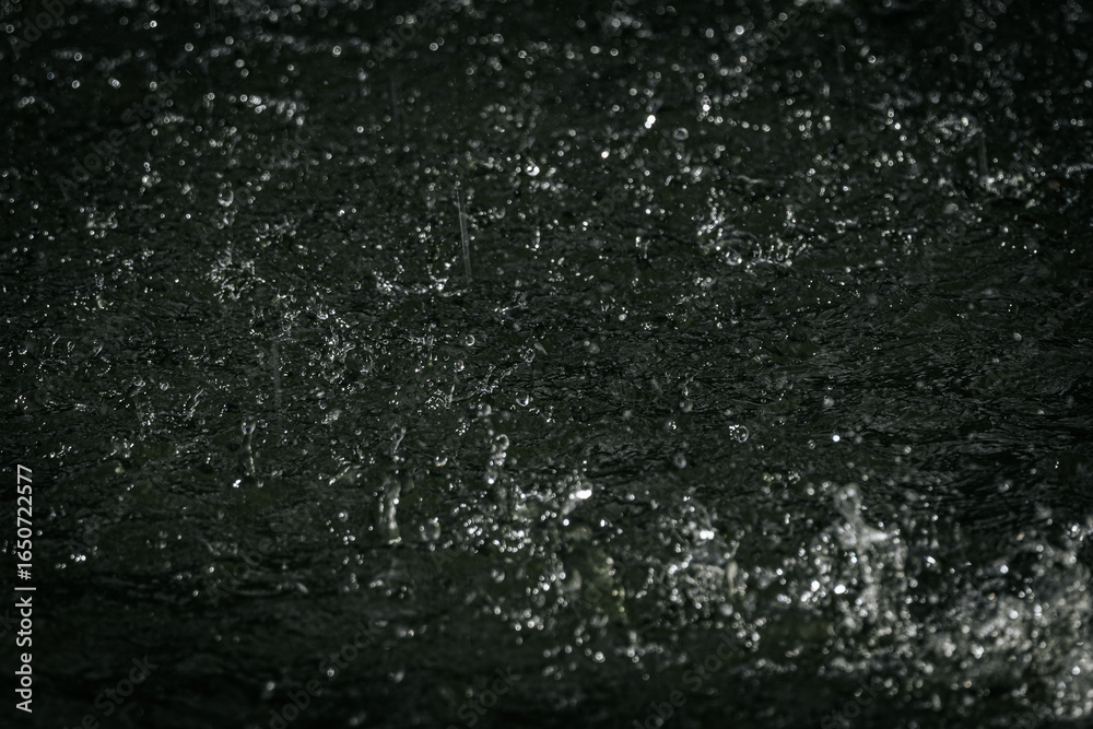 Obraz premium raindrops splashing on water, capturing droplets and ripples in motion with a dramatic, dark background.