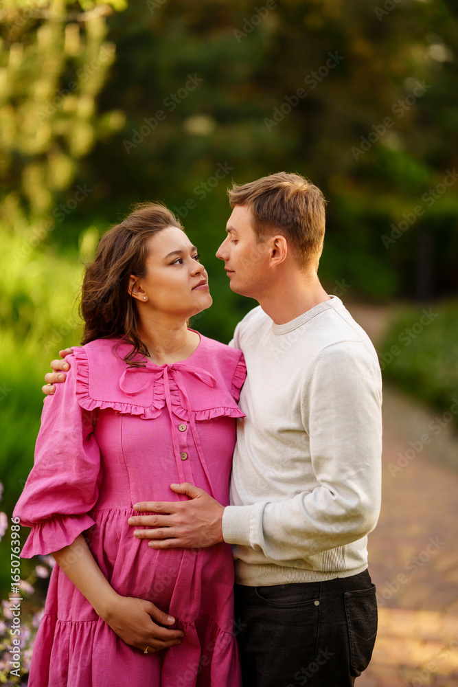 Fototapeta premium Man gently hugging pregnant woman while sitting in garden at home. 
