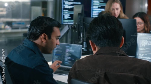 Two Software Developer, Programmer discussing, explaining to colleague working on code, application software development project using desktop computer, work together in co-working office space.