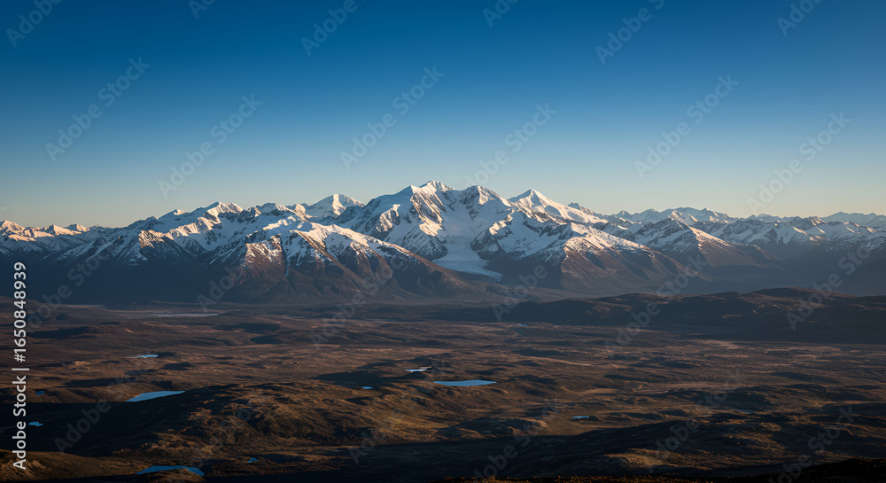 Obraz premium Panoramic view of snow-capped mountain range under a clear blue sky at daytime