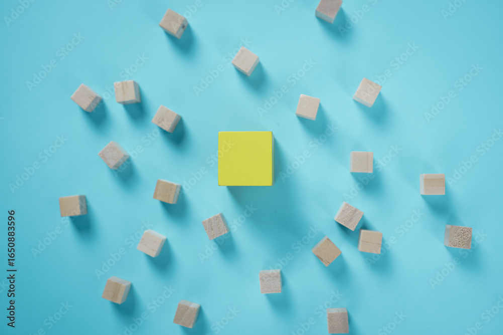 Unique yellow cube standing out among wooden blocks on blue background, concept of leadership, individuality, creativity, innovation, and thinking differently.