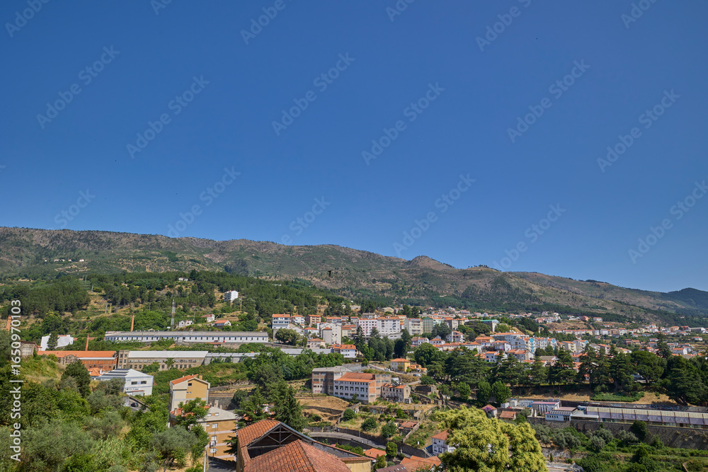 Fototapeta premium Scenic cityscape of Covilha, Portugal with residential buildings, mountains, and clear blue sky.