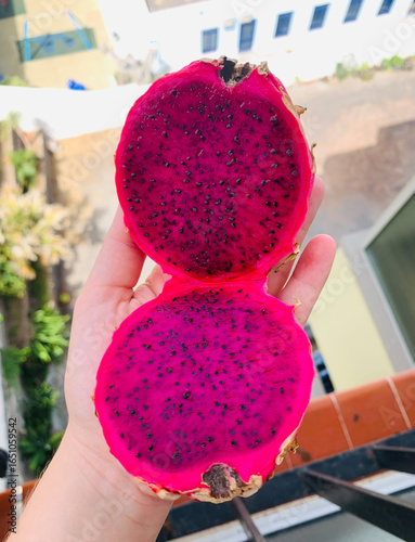 Hand Holding Freshly Cut Dragon Fruit with Vibrant Pink Flesh Outdoors