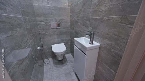 modern bathroom with gray, marble-effect tiles, a white toilet, and a white vanity with a chrome faucet