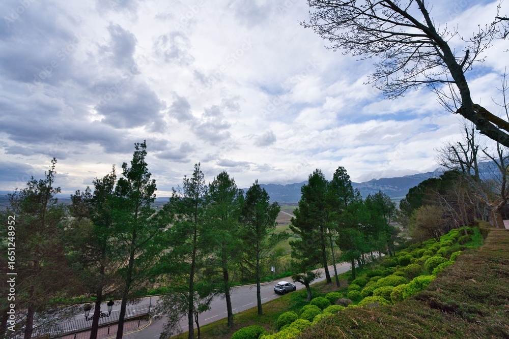 Obraz premium Access road to the town of Laguardia, Basque Country, with its green gardens and the mountain range in the background.