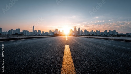 Fototapeta Naklejka Na Ścianę i Meble -  Empty asphalt road leading to a city skyline at sunrise (1)
