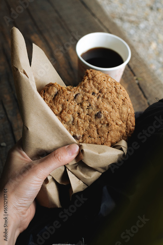 Close up of oatmeal cookie in hand with takeaway coffee