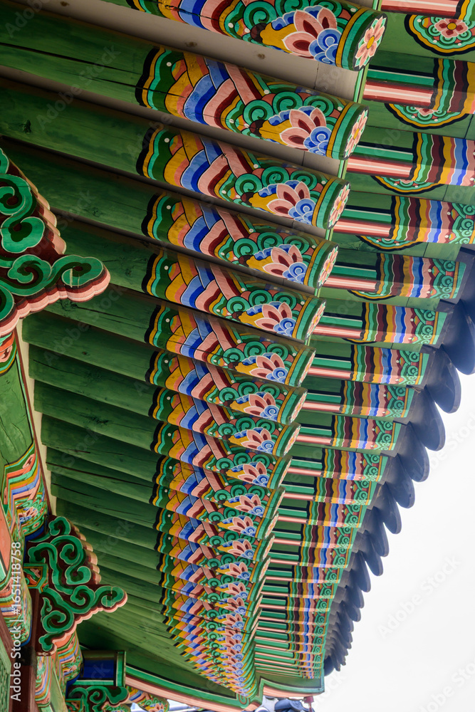Naklejka premium Detailed, colorful eaves of a traditional Korean building at Deoksugung Palace in Seoul, South Korea. Dancheong painting adds ornamentation and protection to wooden surfaces.