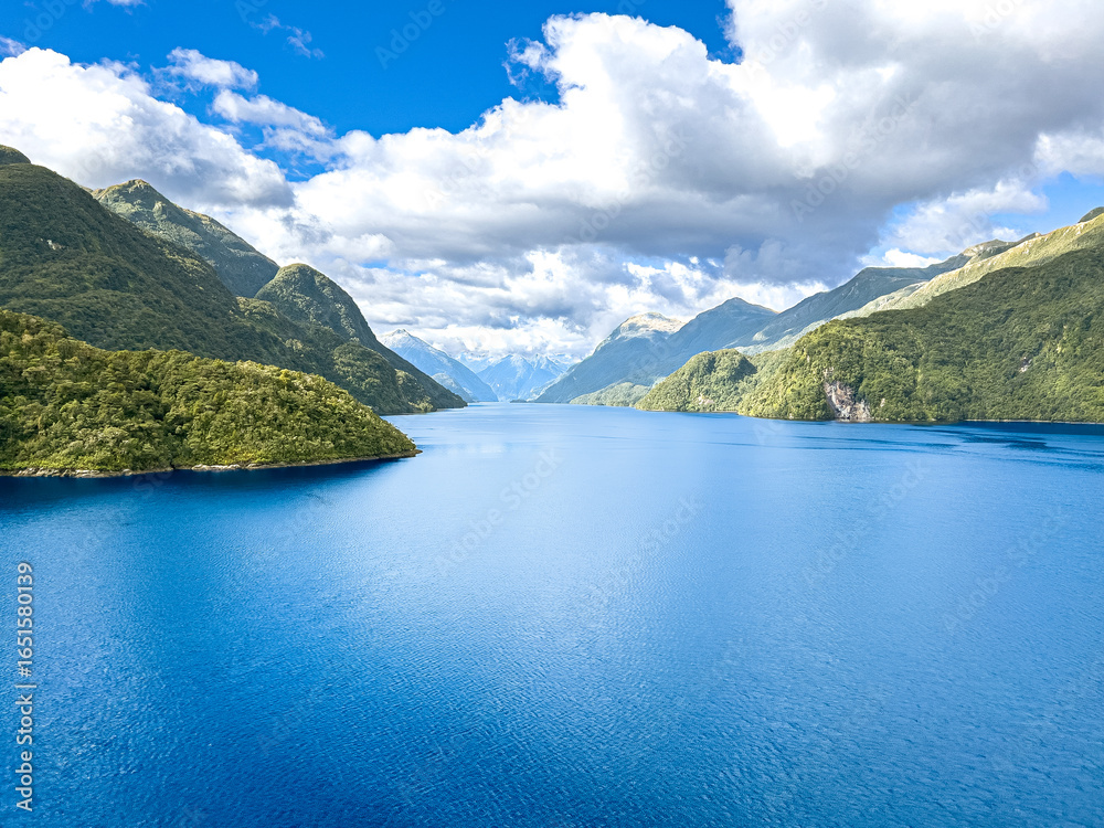 Fototapeta premium Stunning Milford Sound fjord with calm blue waters and lush green hills under a vast cloudy sky, New Zealand