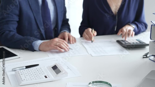Close up of calculator and magnifying glass over financial documents opposite financial team analyzing data, reviewing reports, collaborating at modern office workspace. Audit and taxes in business