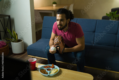 Photography Latin man watching baseball on tv and holding glove and ball