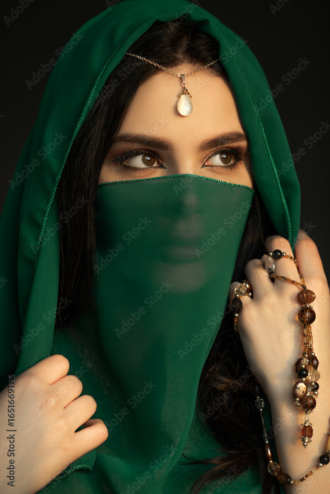 Naklejka premium Mystical Woman in Green Veil With Beads and Pearl Jewelry in Studio
