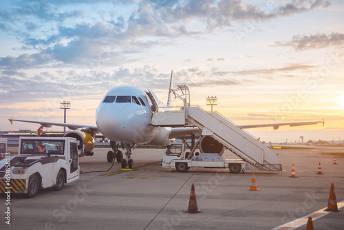 Foto Commercial Airplane On Tarmac At Sunset With Mobile Stairs And Service Vehicles