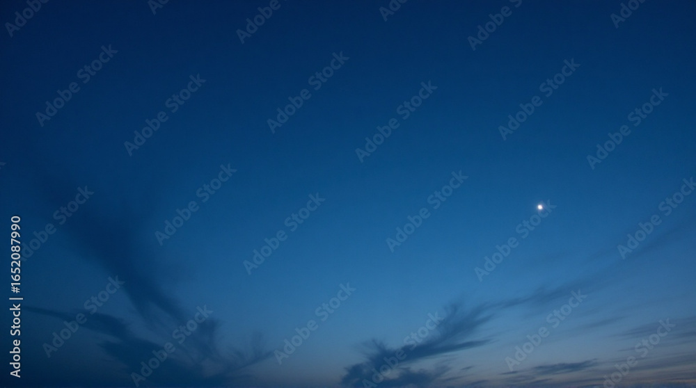 Fototapeta premium Distant planet glows in deep blue twilight sky with wispy clouds stretching across horizon