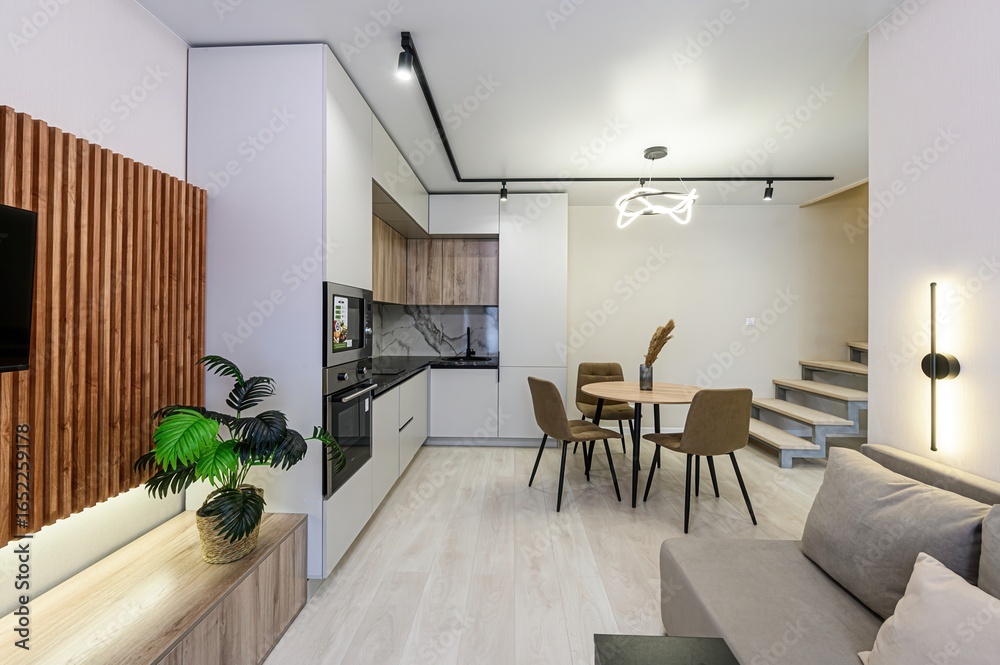 Fototapeta premium modern studio apartment with a kitchen, dining area, sofa, and stairs to a loft. Neutral color palette and minimalist design