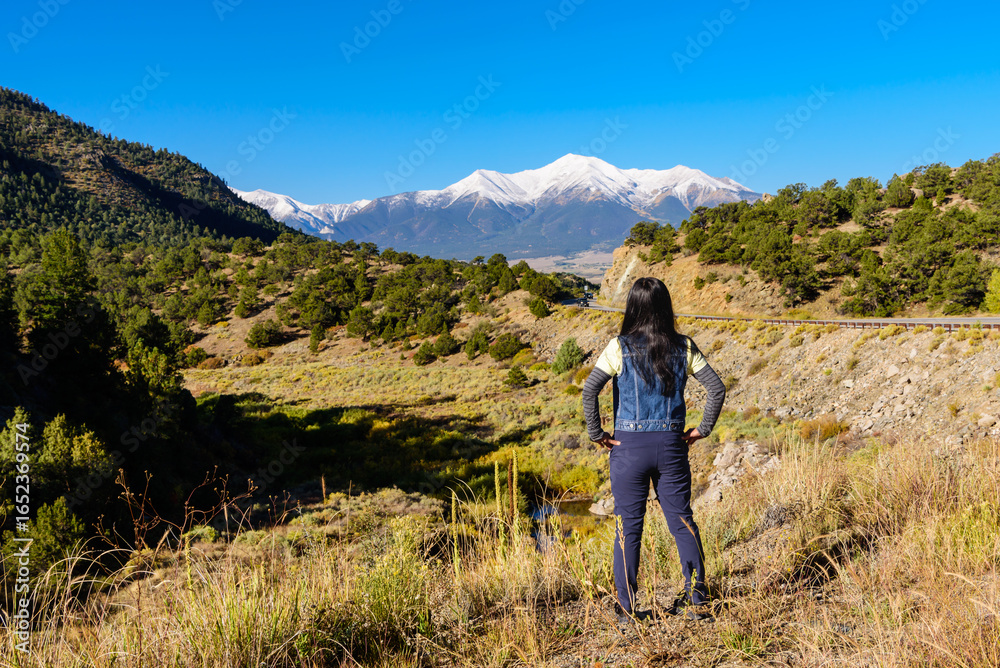 Naklejka premium a traveler stands before Mount Princeton, where blue skies stretch endlessly over Colorado’s autumn roads.