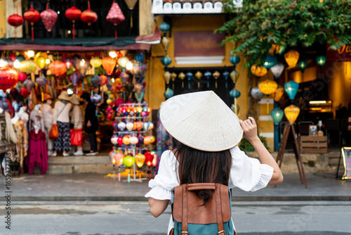 Happy Asian tourist woman wearing Non La (traditional Vietnamese hat) enjoy sightseeing in Hoi An city Vietnam