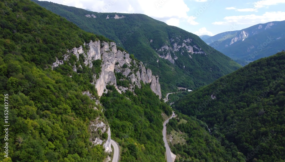 Naklejka premium Winding road through lush green mountains with steep, rocky cliffs