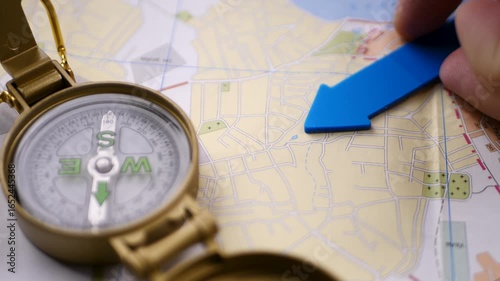 Hand holds brass compass above detailed map. Concept of military operation planning. Tactical decision point. Focus on terrain, coordinates, strategic movement across urban zones