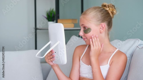 The girl looks in the mirror. The teenager put gel  patches under her eyes.