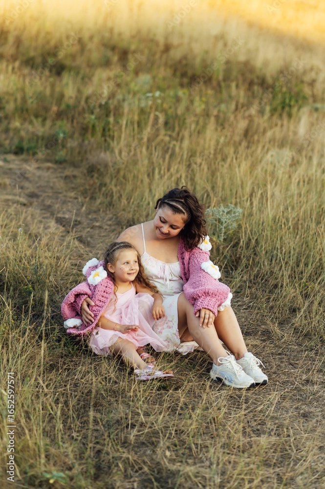 Fototapeta premium A young mother and daughter are hugging in nature among the mountains in beautiful identical sweaters