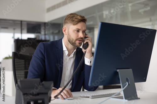 Canvas Print Positive busy young manager man in formal jacket talking on landline phone at of
