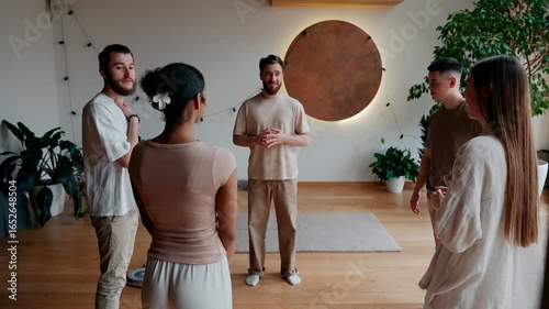 A group of four students and a male yoga mentor talk while standing in a circle