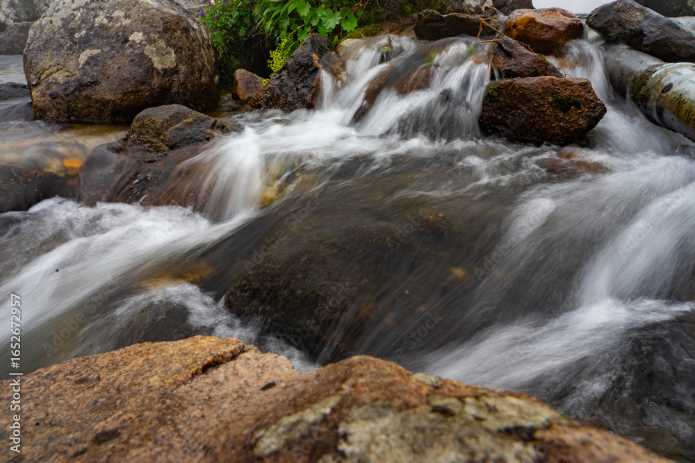 Naklejka premium Pristine mountain stream cascading over rocks in lush landscape