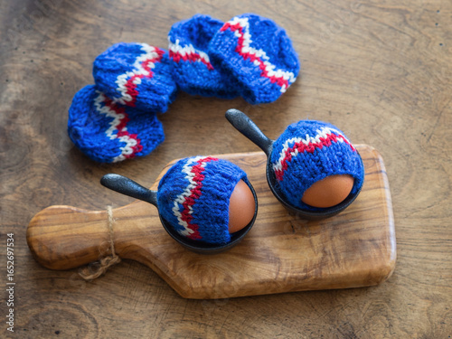 Boiled Eggs with Knitted Blue Egg Warmers on Wooden Board
