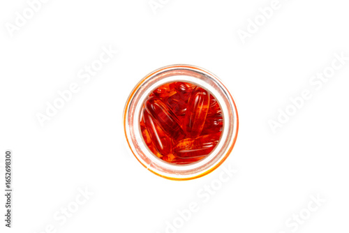 An overhead shot of a clear glass jar filled with red, translucent softgel capsules, isolated on a clean white background, depicting health, medicine, and nutrition.