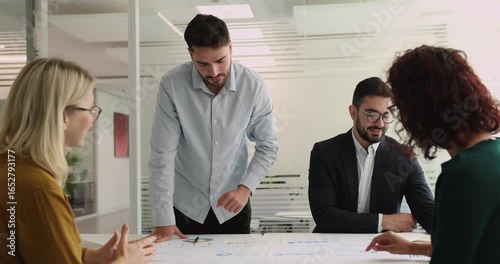 Group engaged in collaborative decision-making in meeting room, reviewing charts and diagrams spread out on conference table, analyze visual data, discussing key metrics, develop data-driven strategy