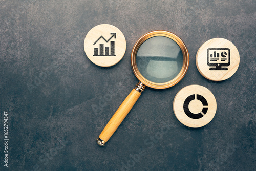 Magnifying glass with wooden circles showing graph chart and computer icon, concept of data analysis, statistics, business intelligence, performance evaluation