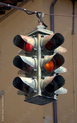 Old 1950s traffic light hanging from a wire showing red and yellow light.