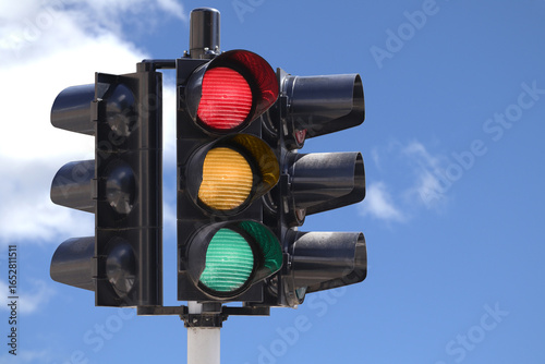 Traffic light with the green, yellow and red light on with the sky as background.