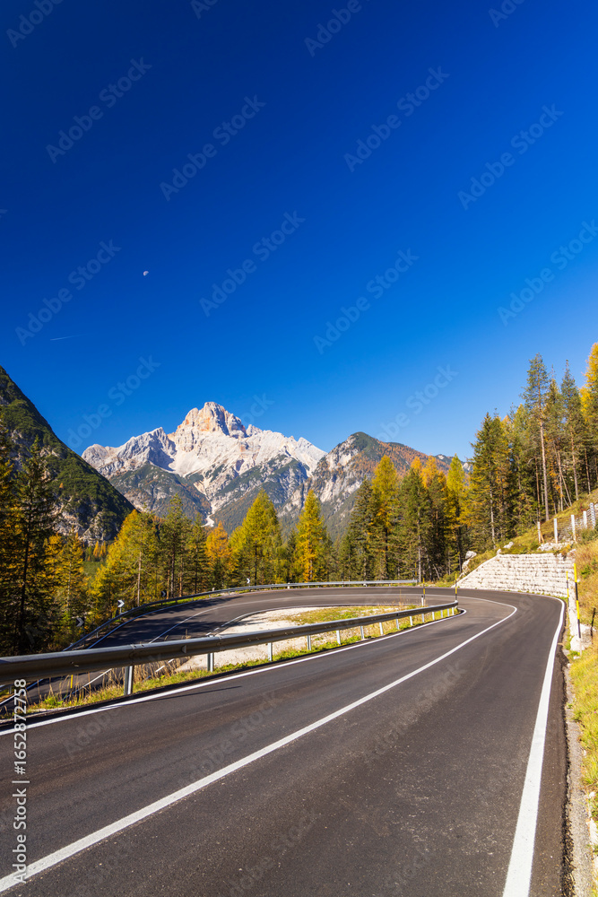 Fototapeta premium Winding mountain road leading to the Dolomites in autumn with a clear blue sky
