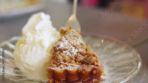 Selective focus, close-up shot of a fork lifting a bite of warm apple crumble pie served with a scoop of creamy vanilla ice cream showing delicious dessert for food, cafes, and sweet treats.
